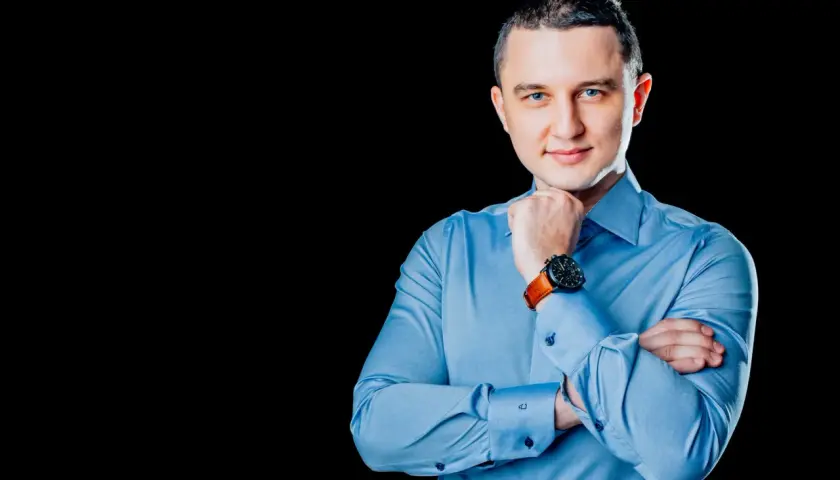 Mężczyzna w niebieskiej koszuli, z rękami skrzyżowanymi na piersi, podczas sesji biznesowej.