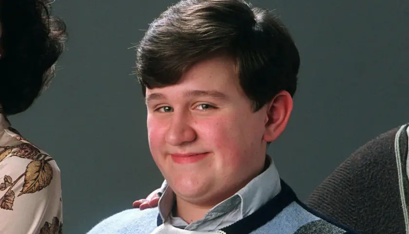 Uśmiechnięty Dudley Dursley, kuzyn Harry'ego Pottera, w niebieskim swetrze.