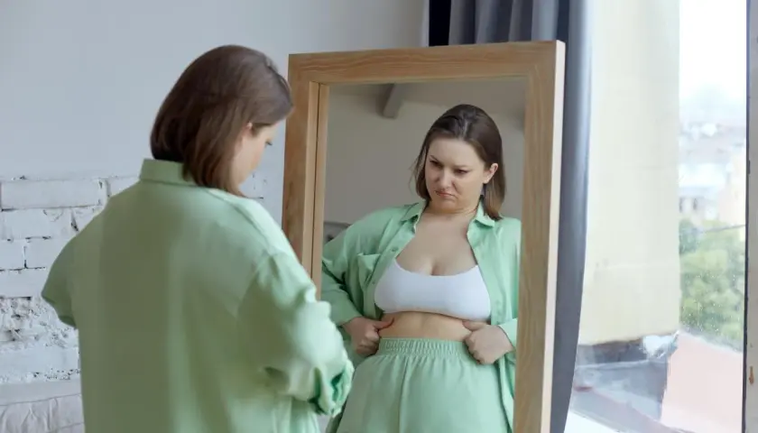 Kobieta w lustrze analizuje swoje ciało, szukając oznak spalania tłuszczu.