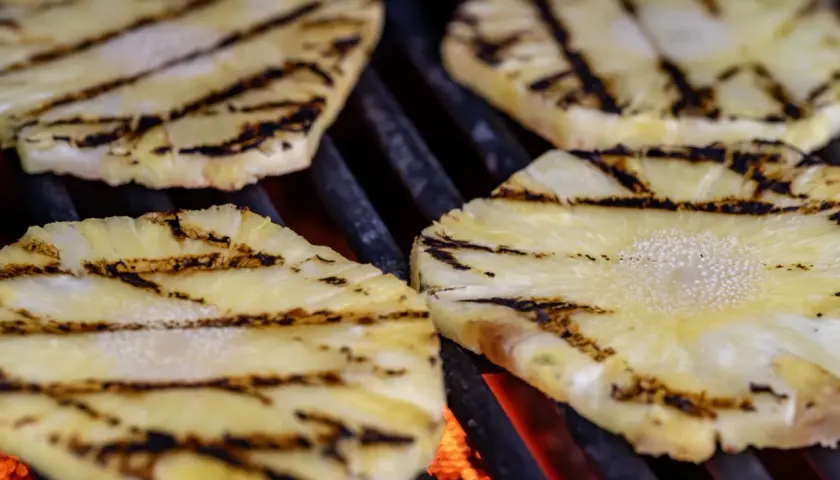 Tranches d'ananas barbecue grillées, avec des marques de cuisson foncées sur fond de braises rougeoyantes.