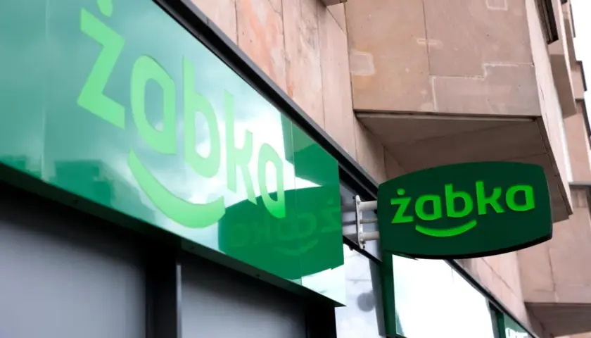Zielony neon z logo Żabki. Zastanawiasz się, od ilu lat można pracować w Żabce? Odpowiedź znajdziesz w tym sklepie.