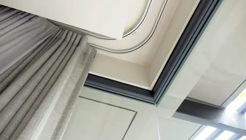 Szyna sufitowa aluminiowa płynnie prowadzi szare zasłony, tworząc elegancką przestrzeń przy dużym oknie.