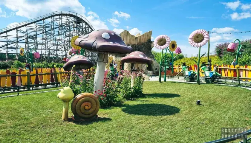 Park rozrywki z kolejką górską, wielkimi grzybami i bajkowymi dekoracjami.
