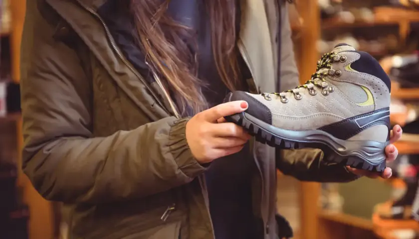 A person in a green jacket holds a hiking boot, considering if boots should fit snug or loose for comfort on the trail.