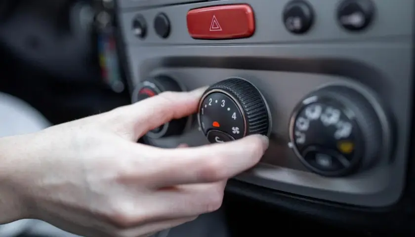 Mano ajustando el control del aire acondicionado a modo frio. El dial muestra números del 1 al 4 y un icono de ventilador.