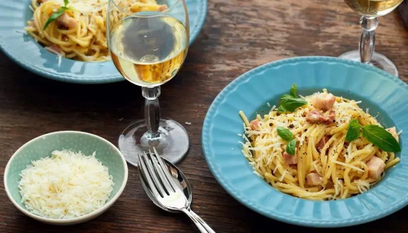 Un délicieux vin blanc accompagne un plat de spaghetti carbonara, garni de parmesan râpé et de basilic frais.