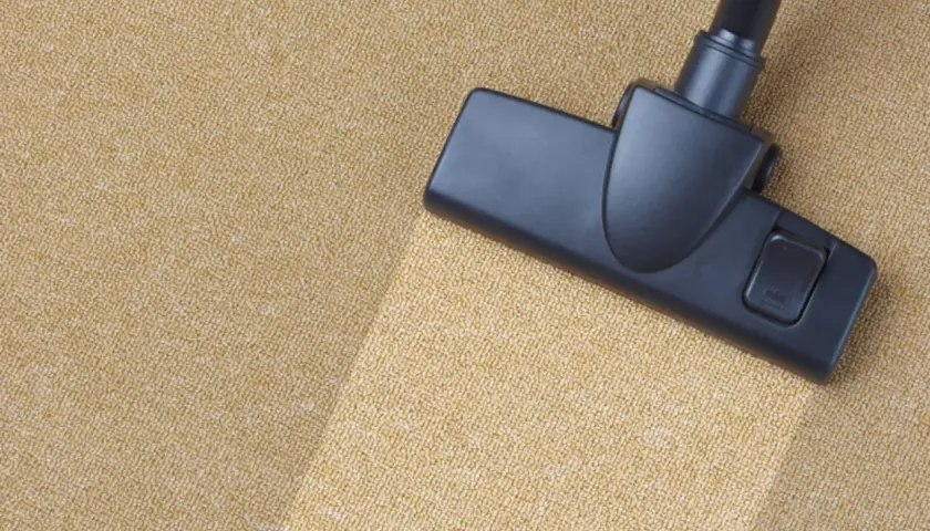 Cabezal de aspiradora limpiando una alfombra beige. Un ejemplo visual de como limpiar una alfombra para dejarla impecable.