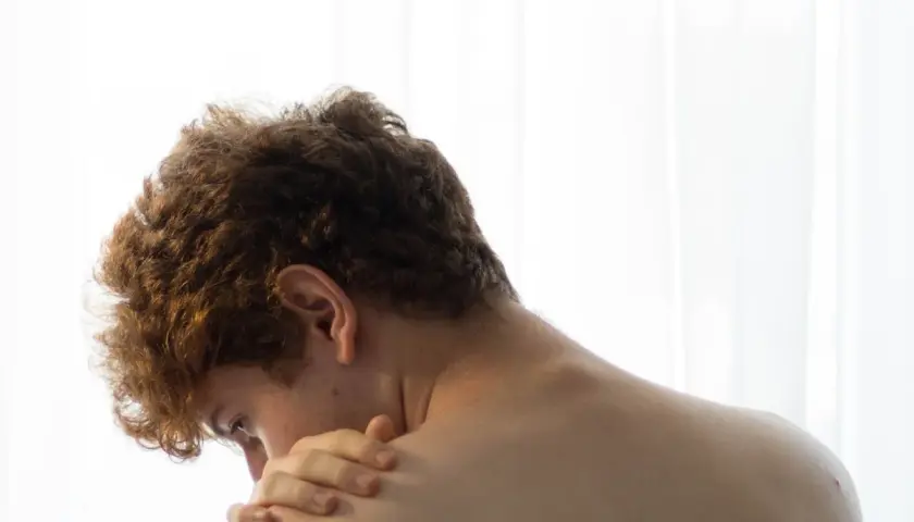 Close-up of a young person's back and neck, with a hand touching their shoulder.