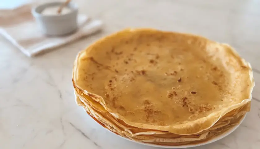 Pile de crêpes dorées, parfaites pour une recette crêpe moelleuse. Un petit bol de sucre est à côté.