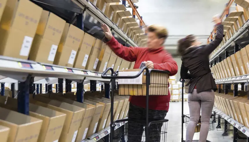 Mitarbeiter im Lager führen pick & pack aus, greifen Kartons aus Regalen und legen sie in Wagen.