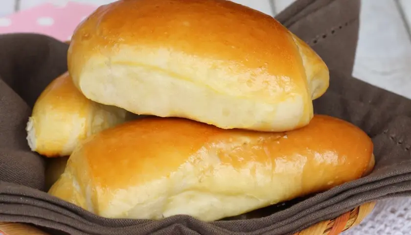 Deliziosi panini al latte dorati, morbidi e invitanti, serviti in un cestino foderato con un tovagliolo marrone.