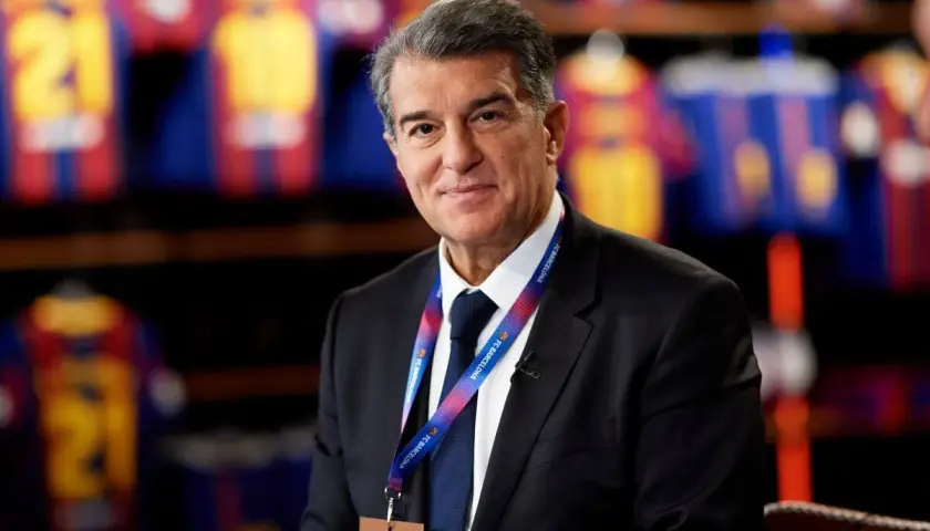 Prezes FC Barcelona, Joan Laporta, w garniturze, z identyfikatorem klubu na szyi, na tle klubowych koszulek.