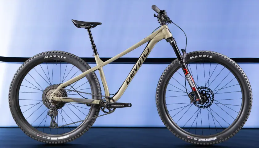 A tan Devinci Kobain mountain bike with Maxxis tires and a Marzocchi Bomber fork, ready for any trail.