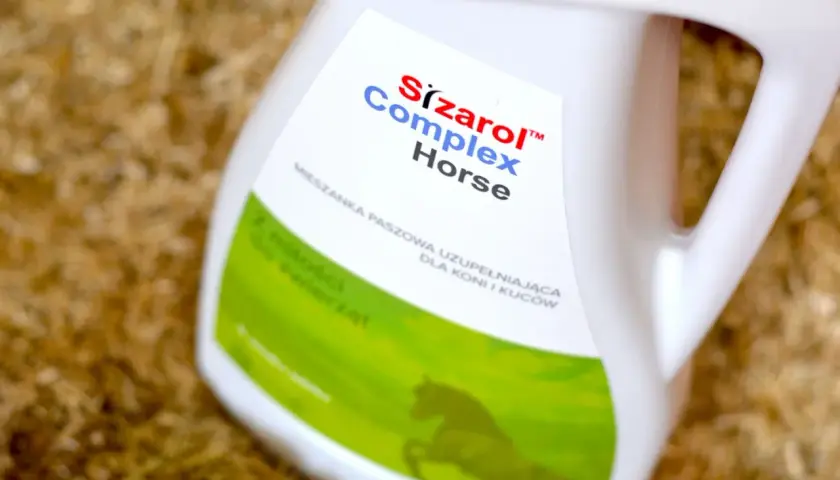 Biały kanister z etykietą "Sizarol Complex Horse" na tle ściółki dla zwierząt.