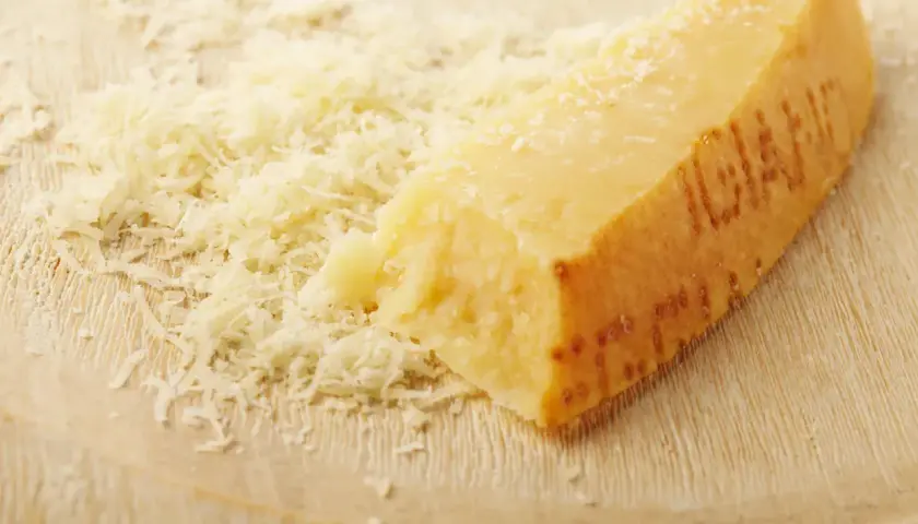 Ein Stück Parmesan mit geriebenem Käse daneben. Die Rinde ist deutlich geprägt und zeigt, dass die **Parmesanrinde essbar** ist.