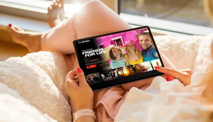 Kobieta ogląda na tablecie seriale do nauki angielskiego B1. Na ekranie tytuł "Friends for Life" i zdjęcie uśmiechniętych ludzi.