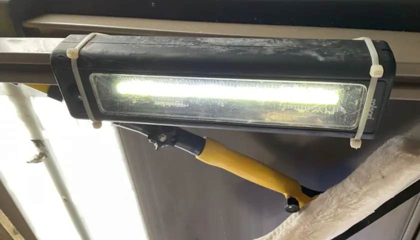 Jasne, oto opis:

Oświetlenie garażu bez prądu: prowizoryczna lampa LED na opaskach zaciskowych, oświetlająca wnętrze. Obok wisi narzędzie do czyszczenia.