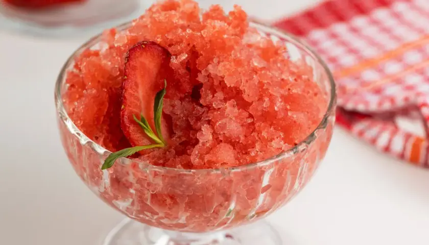 Sorbet truskawkowy w pucharku, ozdobiony plasterkiem truskawki i miętą.