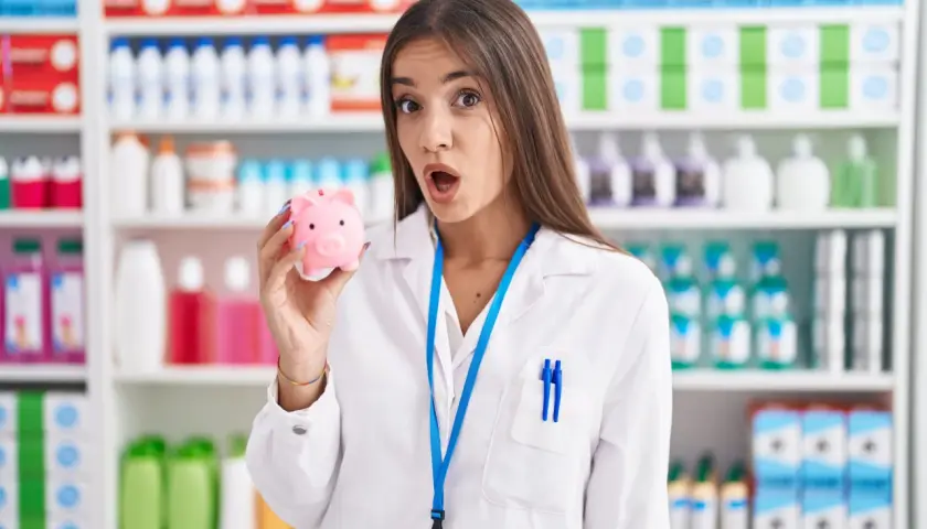 Zaskoczona farmaceutka trzyma skarbonkę, zastanawiając się, ile zarabia technik farmacji.