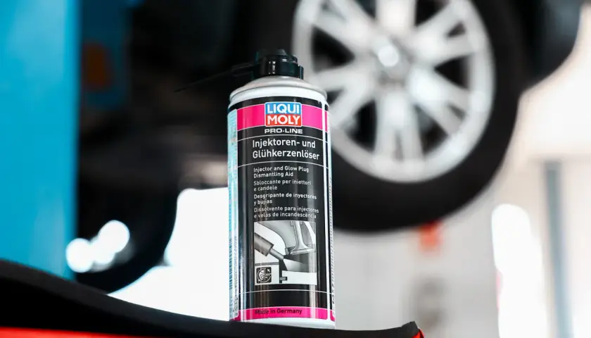 Puszka preparatu do czyszczenia wtryskiwaczy Liqui Moly na tle koła samochodu. Pomaga w demontażu zapieczonych elementów.