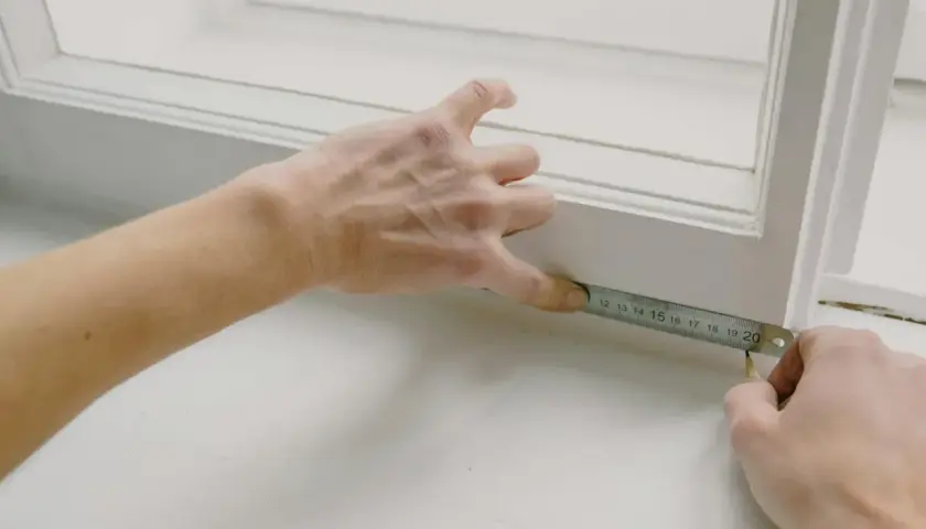 Ręce mierzą długość porysowanego parapetu z blachy.