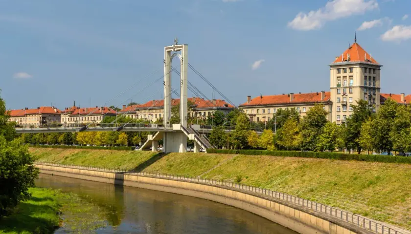 Most nowoczesny nad rzeką w Kownie starówka, z charakterystyczną wieżą i budynkami z czerwonymi dachami w tle.