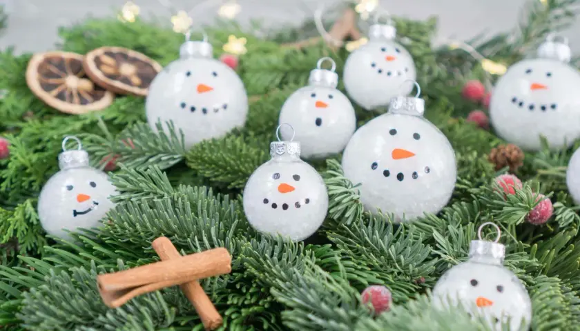 Schneemann-Weihnachtskugeln bemalen: süße Ideen für DIY-Deko. Tannengrün, Zimtstangen und getrocknete Orangen ergänzen die winterliche Szene.