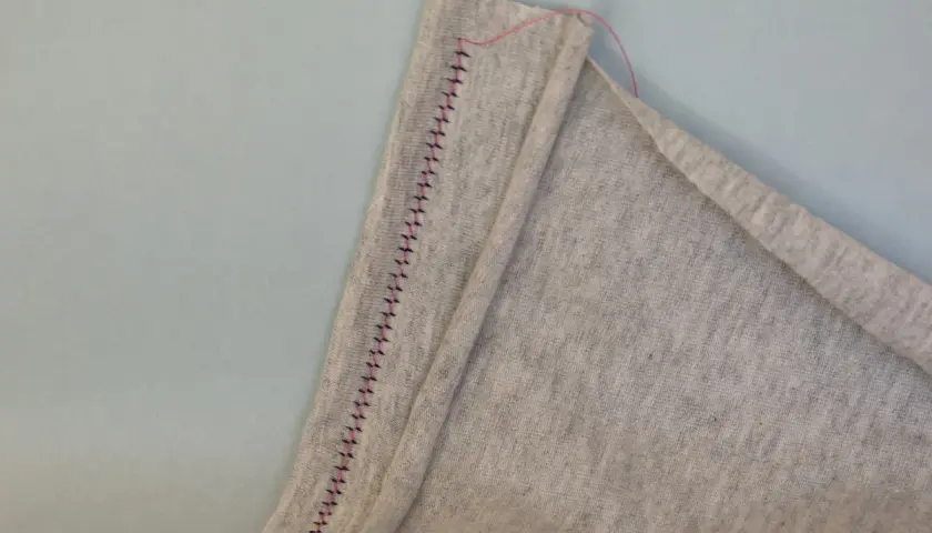 A close-up shows a grey fabric hem stitched with a twin needle, creating a decorative zigzag pattern.