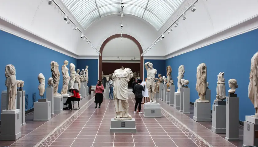 Wnętrze muzeum z rzeźbami antycznymi. Wśród zwiedzających artystka szkicująca posąg. Warto odwiedzić muzea w Krakowie.