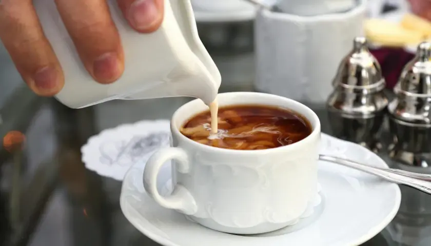 Ein Schwall Milch fließt in eine Tasse filterkaffee mit milchschaum. Ein Moment der Ruhe vor dem ersten Schluck.