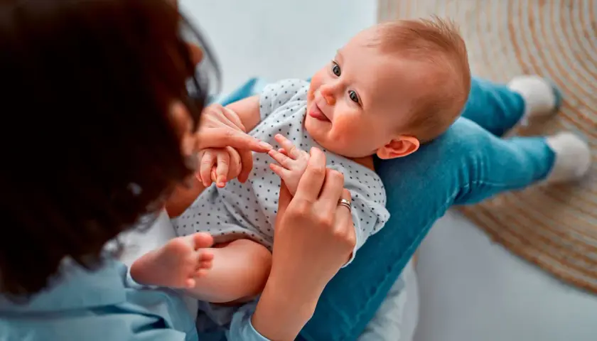 Madre juega con su bebé, enseñándole sus deditos. El bebé sonríe, quizás practicando sus primeras palabras.