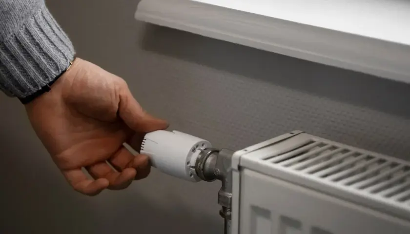 Dłoń regulująca termostat grzejnika w mieszkaniu.