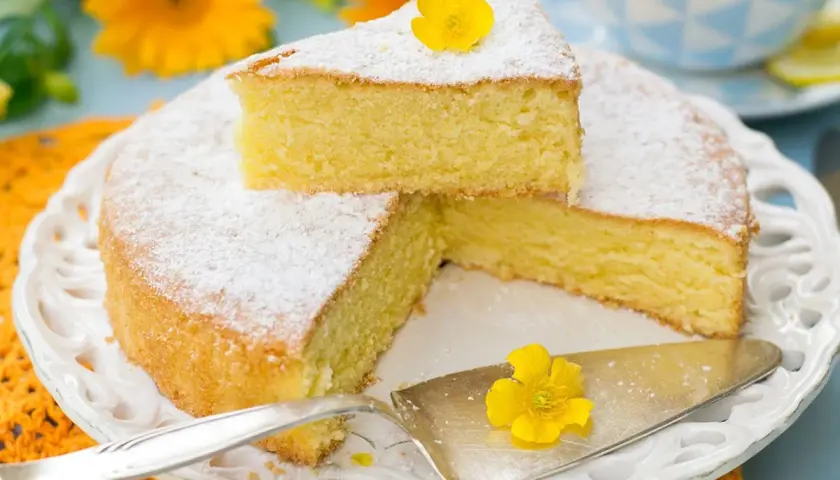 Una torta paradiso sofficissima, spolverata di zucchero a velo e decorata con un fiore giallo, pronta per essere gustata.