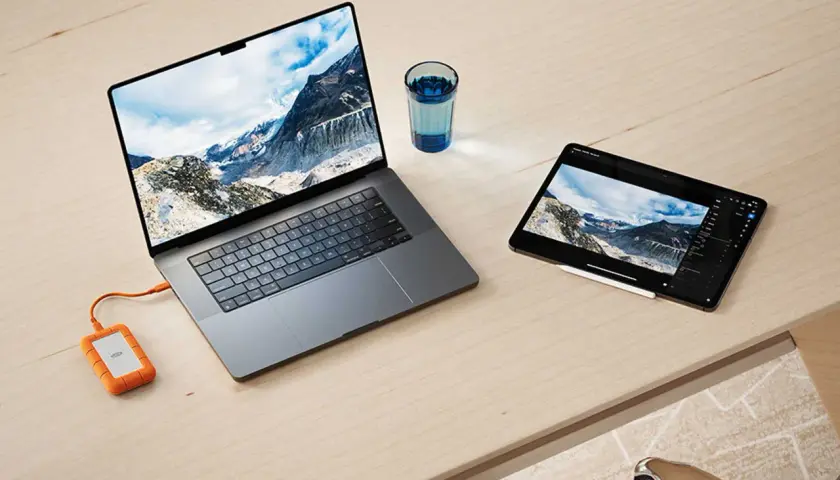 Ein Laptop und ein Tablet mit Berglandschaft, verbunden mit einer externen Festplatte. Ideal für den Datenaustausch zwischen exFAT Windows und Mac.