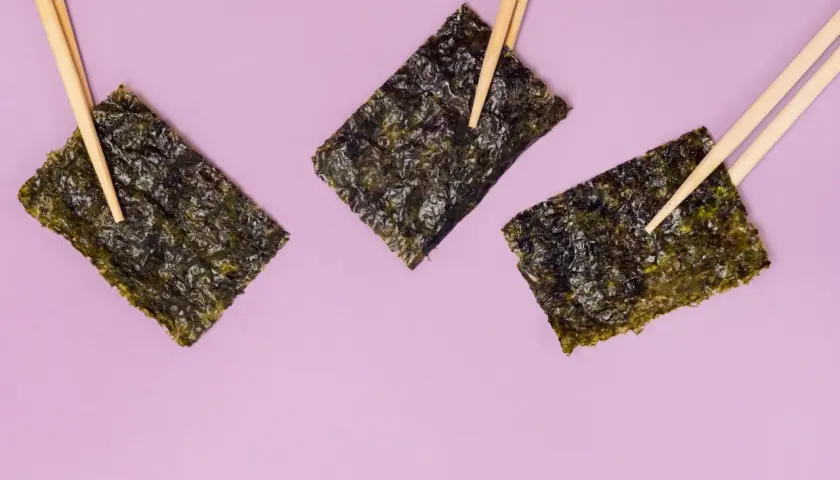 Tre fogli di alga nori, tenuti da bacchette, evidenziano le loro proprietà nutritive.