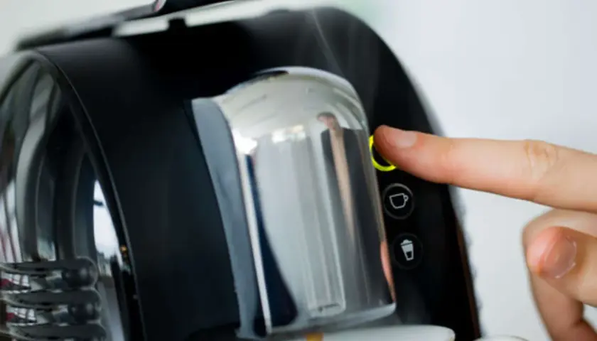 Finger drückt Knopf an Kaffeemaschine. Zeit, den Kaffeeautomaten zu entkalken für perfekten Kaffeegenuss.