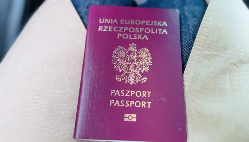 Polski paszport leżący na jasnym płaszczu i dżinsach.