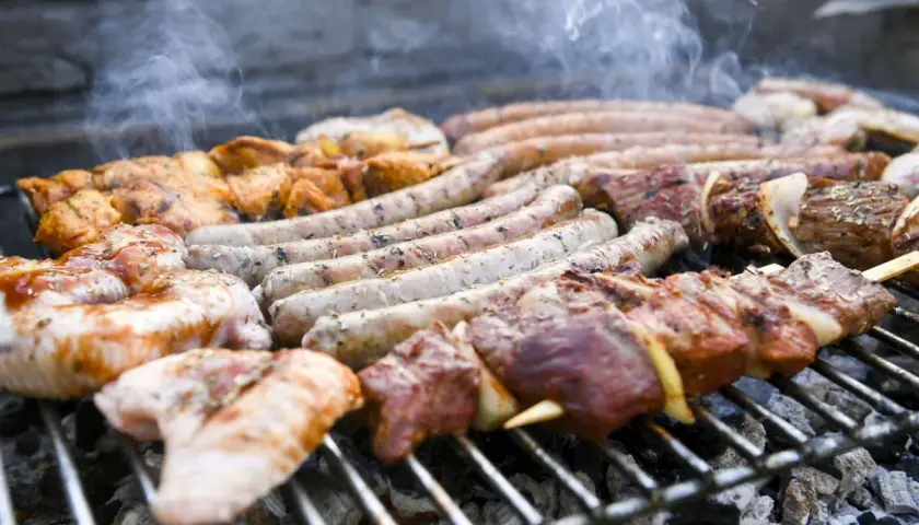 Des saucisses, brochettes de viande et morceaux de poulet à faire un barbecue sur un gril chaud, avec de la fumée qui s'échappe.