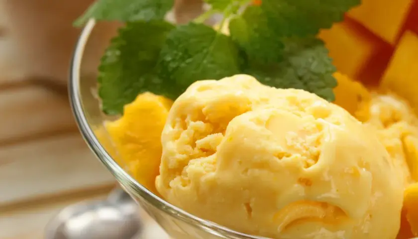 Domowe lody mango z miętą w szklanej miseczce.