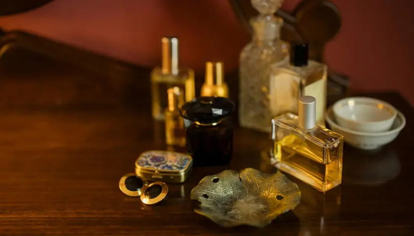 Eleganckie flakoniki z perfumami i woda kolońska co to? Na drewnianym blacie stoją różne rodzaje perfum, spinki do mankietów i ozdobna szkatułka.
