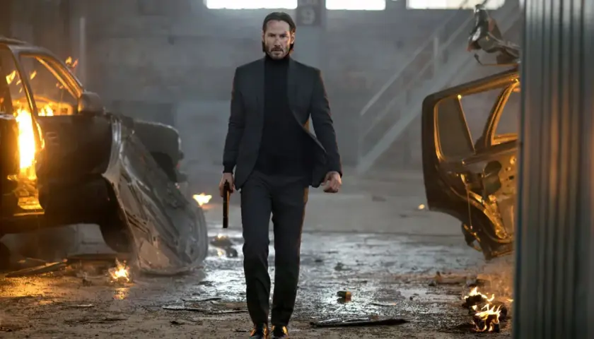 John Wick, med en pistol i handen, går genom ett inferno av brinnande bilar. En scen från rollistan i John Wick.