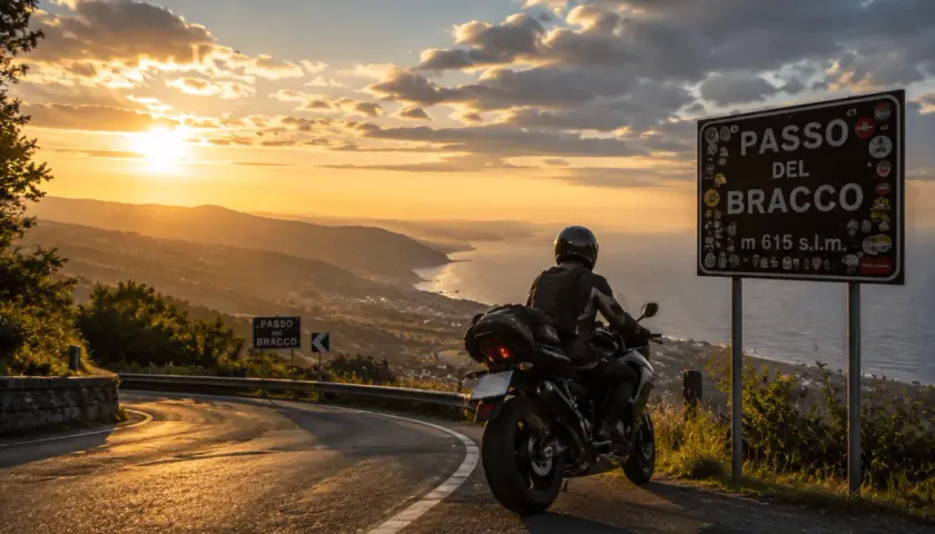 Motociclista ammira il tramonto sulle **strade panoramiche Liguria in moto**. Segnale del Passo del Bracco.