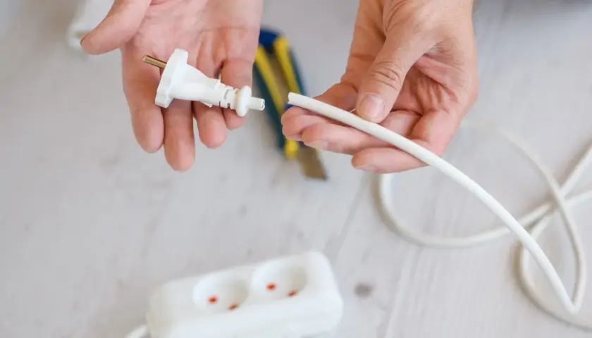 Dłonie przygotowują kabel do podłączenia do wtyczki z uziemieniem. W tle widać listwę zasilającą.