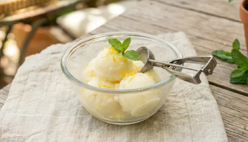 Un délicieux sorbet citron sans sorbetière, garni de menthe fraîche et de zestes de citron, servi dans un bol en verre.