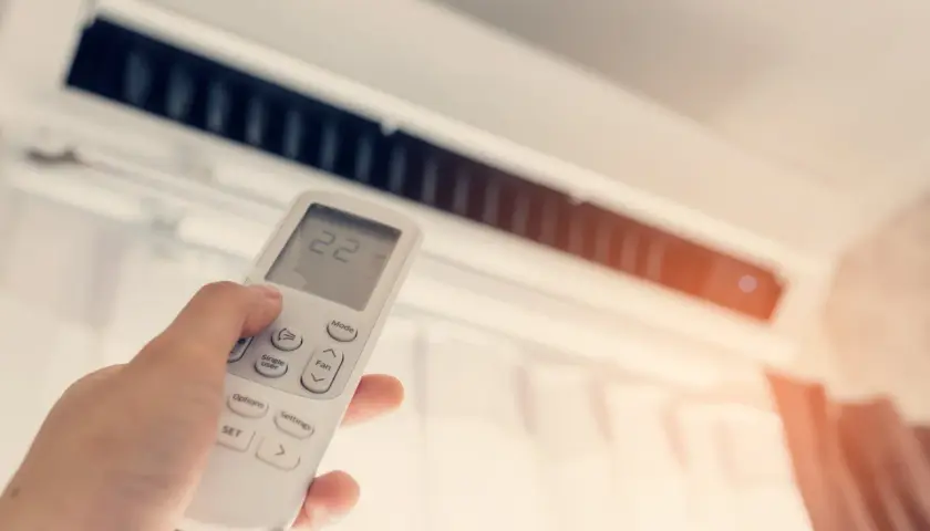 Mano sujetando control remoto de aire acondicionado para combatir el calor. La pantalla muestra 22 grados.