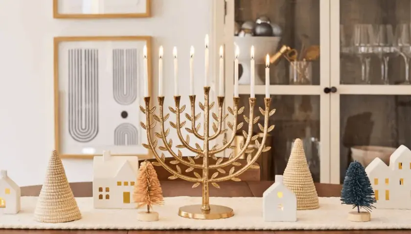 A golden menorah with lit candles is the centerpiece of this Chanukah decorating idea, surrounded by miniature houses and trees.
