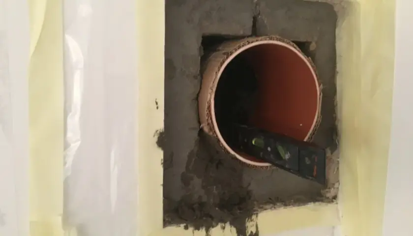 Inmurningsstos montering. Ett rör sitter i en betongvägg, en vattenpass kontrollerar att det är rakt.