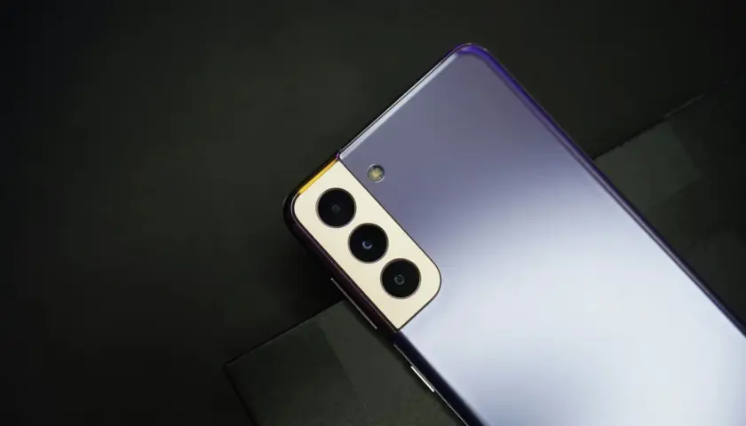 Fioletowy Samsung S21, rok produkcji 2021, z potrójnym aparatem i złotą ramką, leży na czarnym tle.