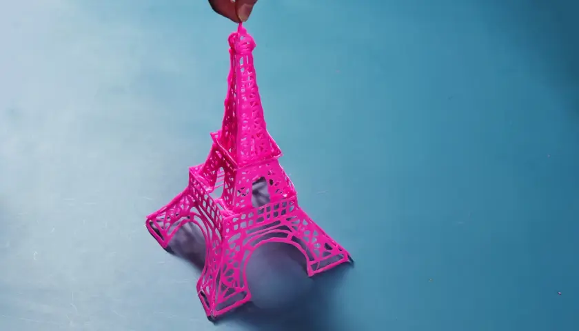 Una manualidad de la Torre Eiffel rosa, creada con filamento, sostenida por un dedo.