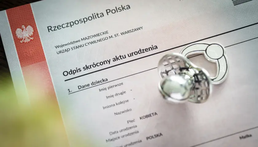 Odpis aktu urodzenia z Polski, obok smoczek. Dokument zawiera dane dziecka, w tym miejsce na wpisanie imion, które mogą być jednymi z najpopularniejszych imion.